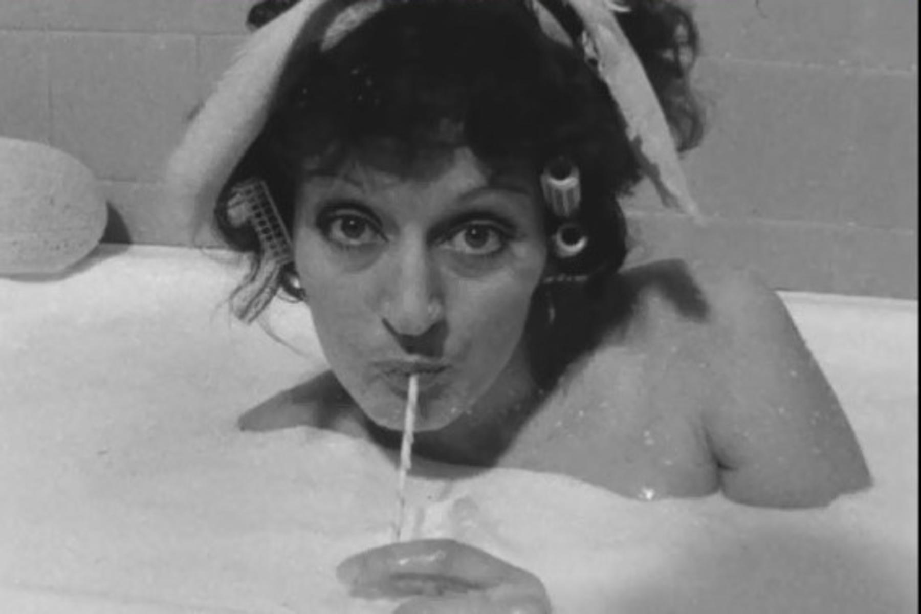 Black white film still of Germaine Greer immerser in bathtub filled with milk with straw in mouth