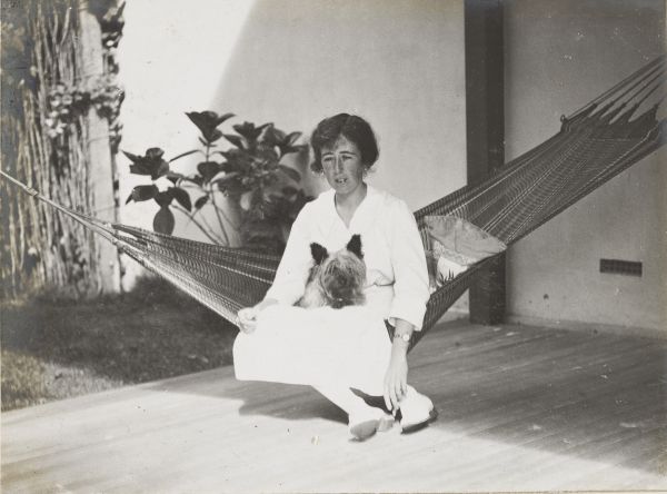 Woman sitting on hammock with feet planted on ground, terrier dog in her lap