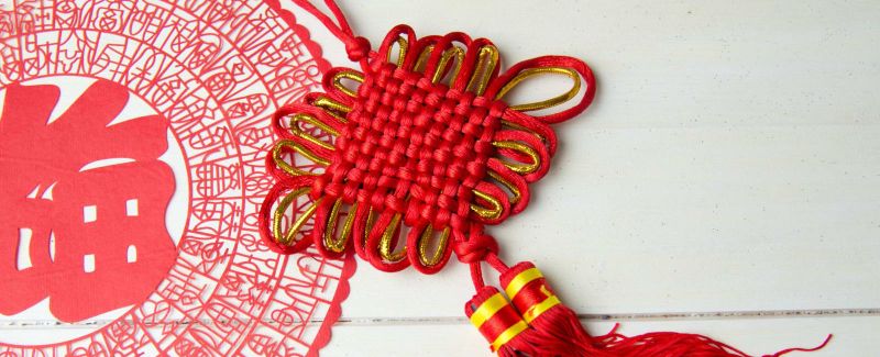 Image of a traditional red Chinese woven knot, against a red decorative image.