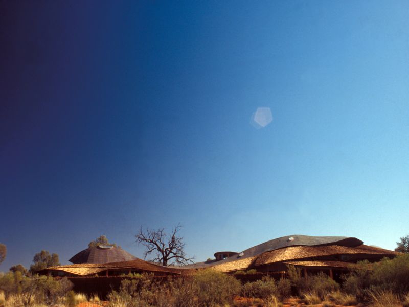 Curvy building set amongst large blue sky, with shining sun, in Australian desert setting