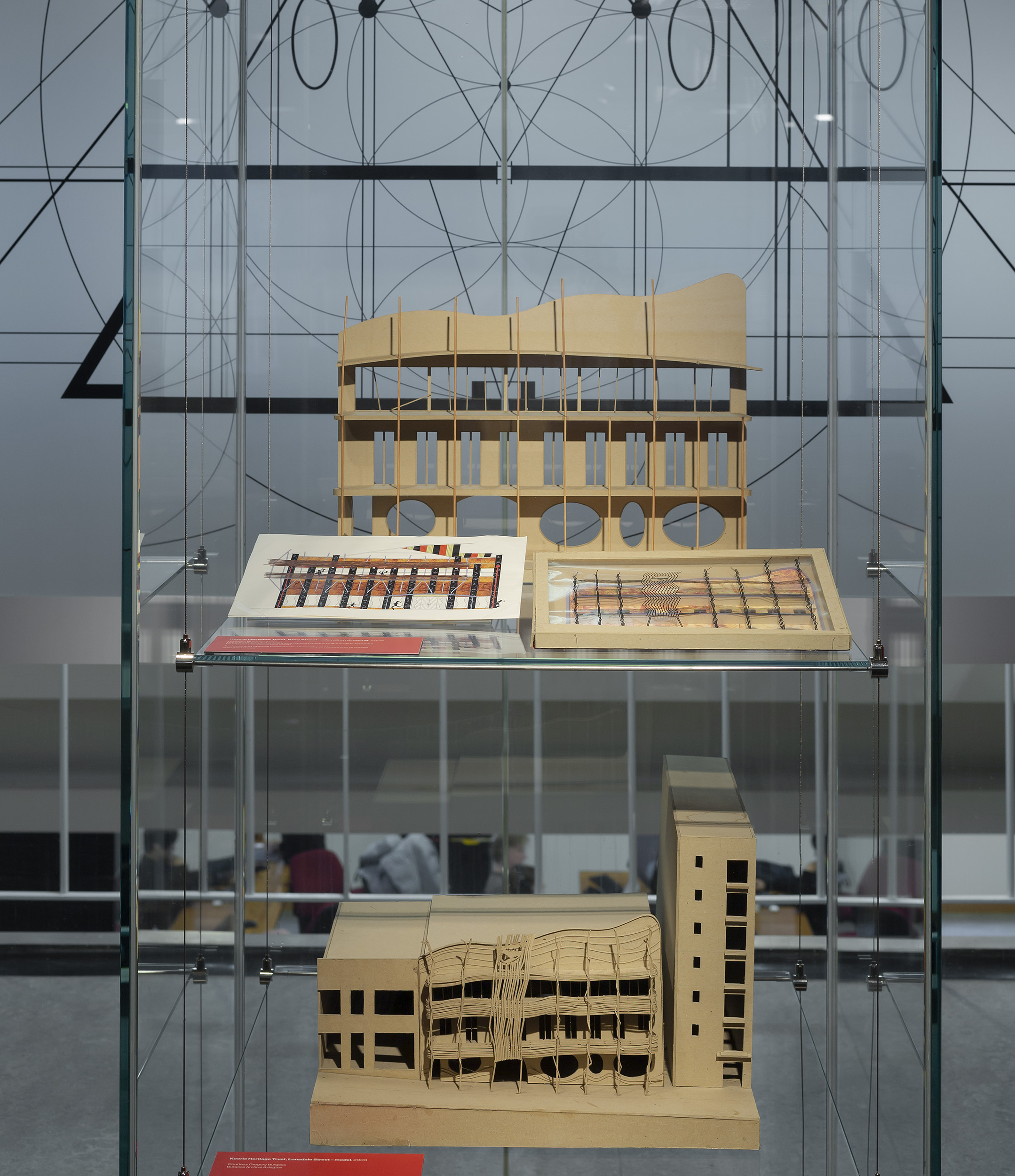 Glass exhibition display case featuring two architectural models, built from cardboard