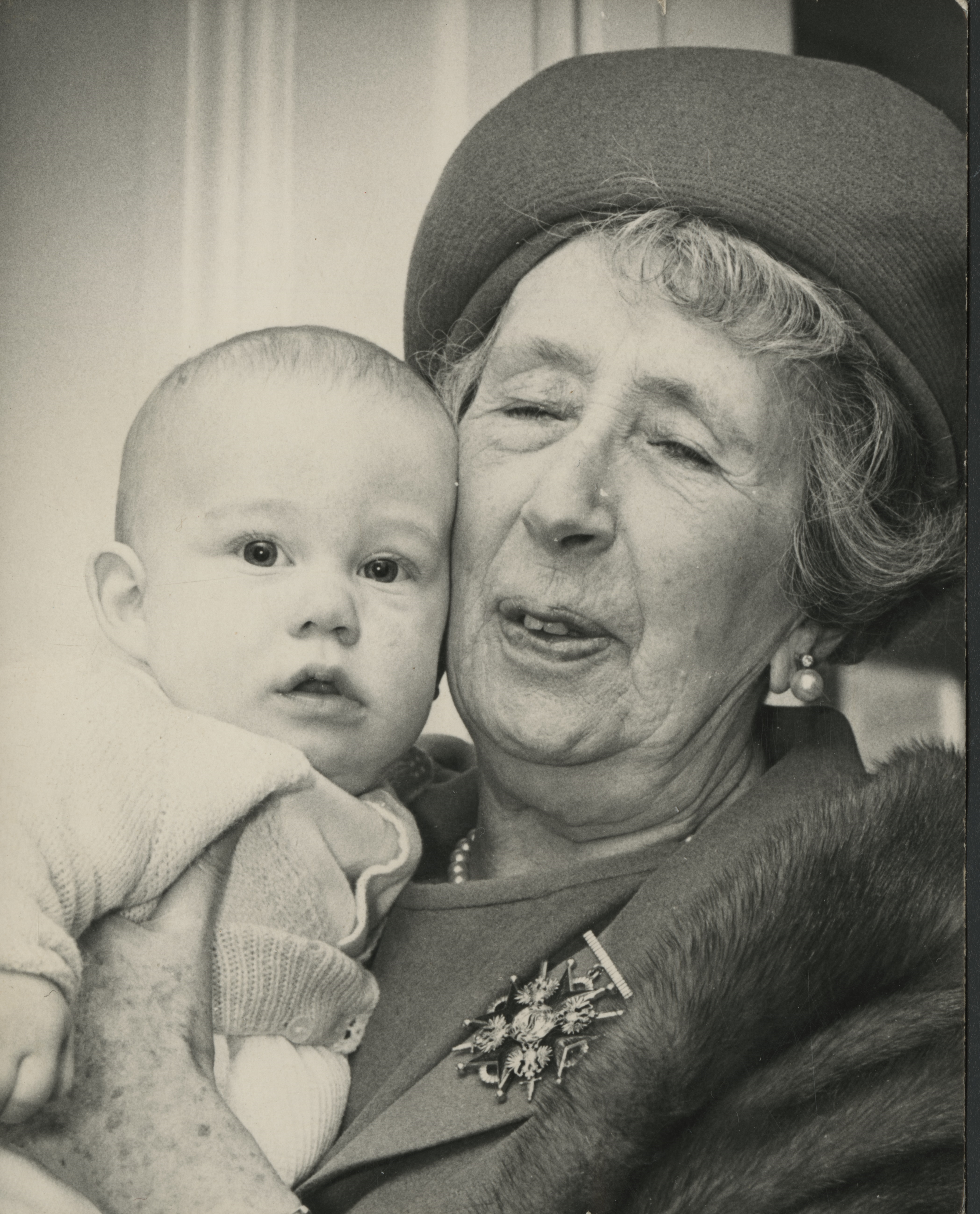 Older woman wearing box hat holding baby and smiling 