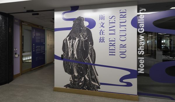 Photograph of an exhibition entry wall with large figure in black vinyl with text running vertically