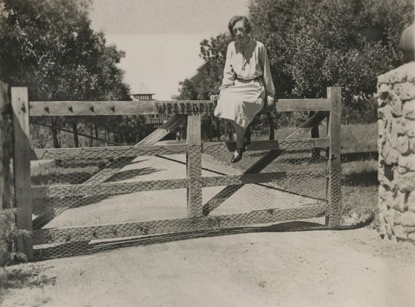 woman sitting on farm driveway slatted timber gate 