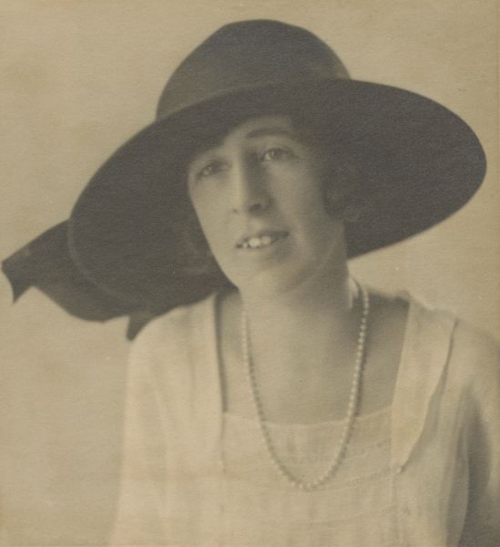 Head and shoulders portrait of young woman in wide brim hat and pearls 