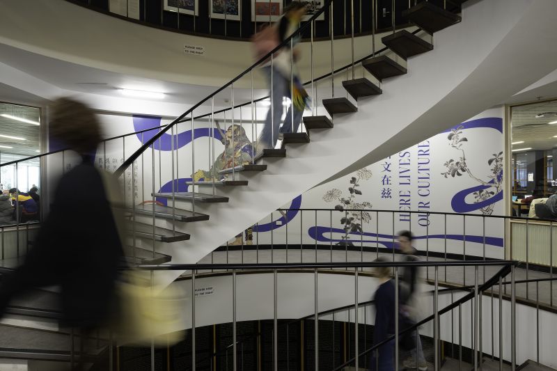 People walking up and down spiral staircase with decorative vinyl on staircase wall