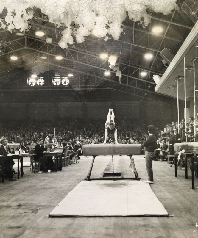 Photograph of the Olympic Games 1956, Melbourne stadium. Female gymnast performing vault routine. Photographer unknown.