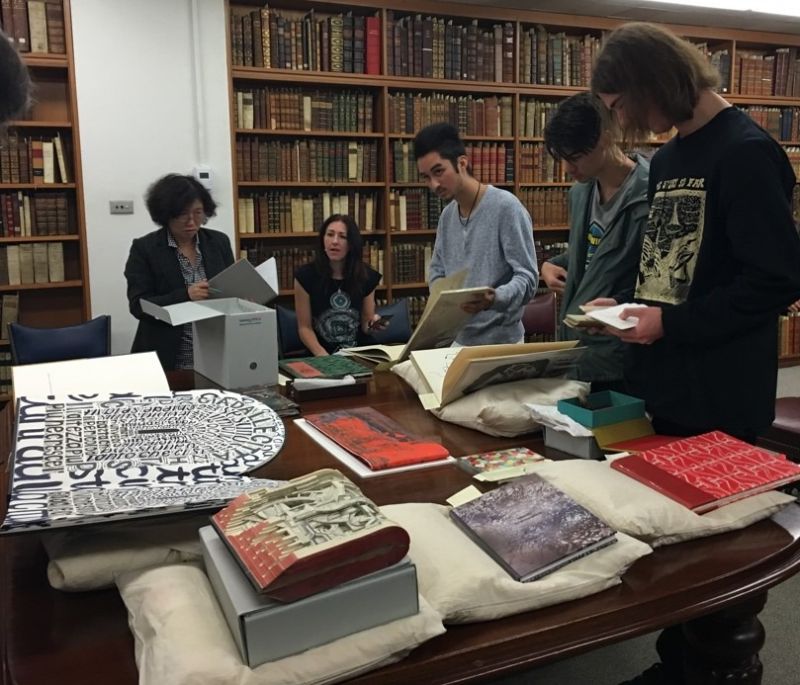 A group of young people examining a table of artist books on black pillows
