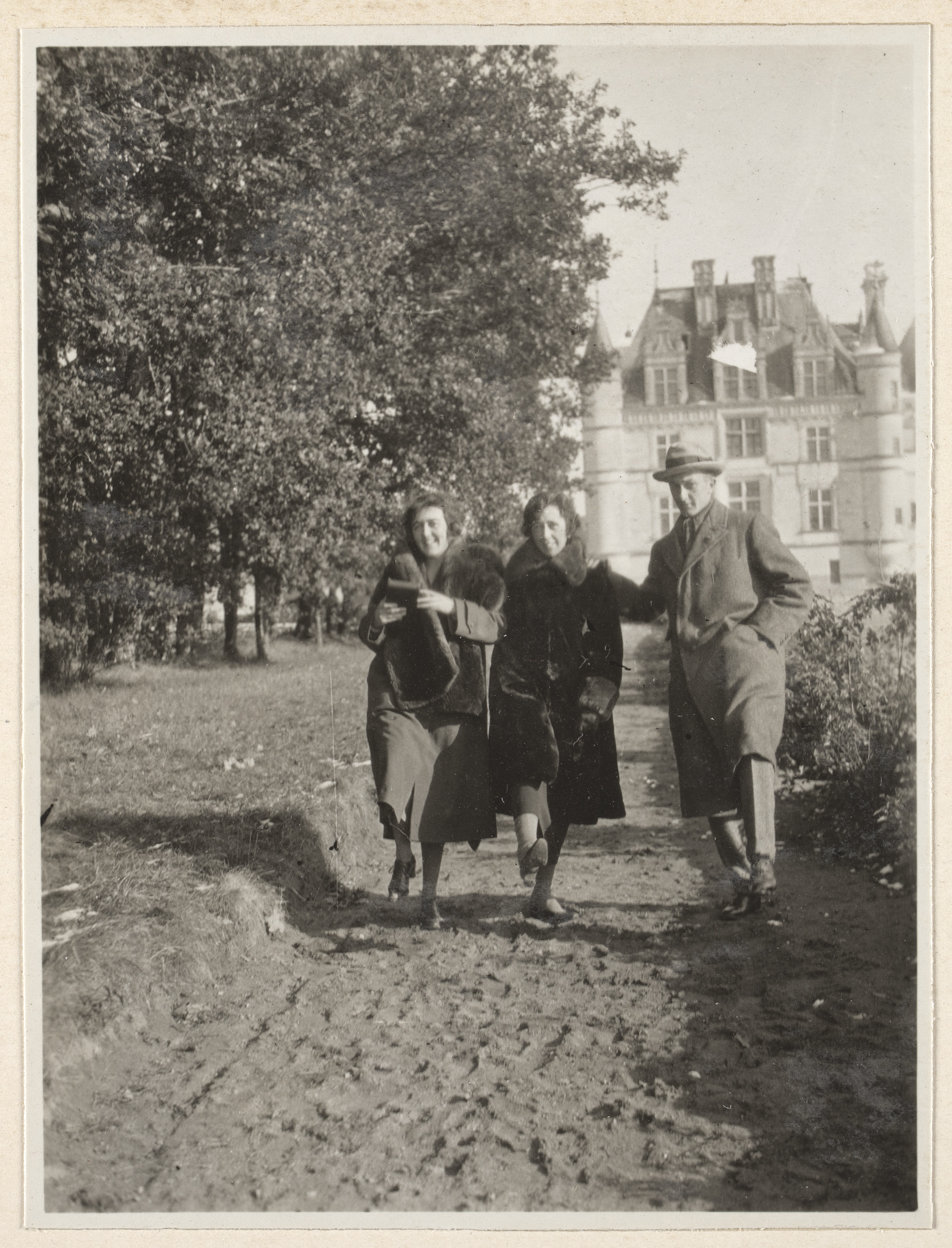 Two women and one man dressed in winter coats skipping down path, Chenonceau Château in background