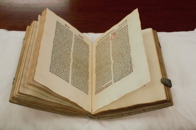 Open faced very aged book with yellowed pages, on white book pillow