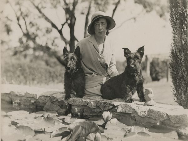 woman dressed in hat and coat sitting with two Scottish Terrier dogs in Australian 