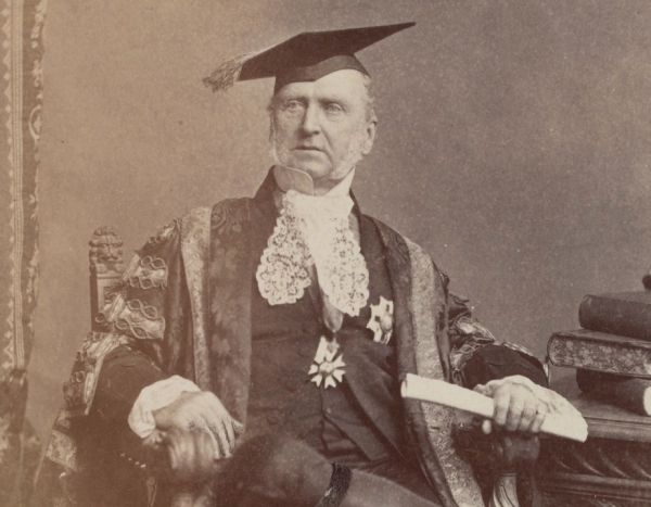 Portrait of Sir Redmond Barry seated and wearing long Chancellor's robes and a square academic cap.